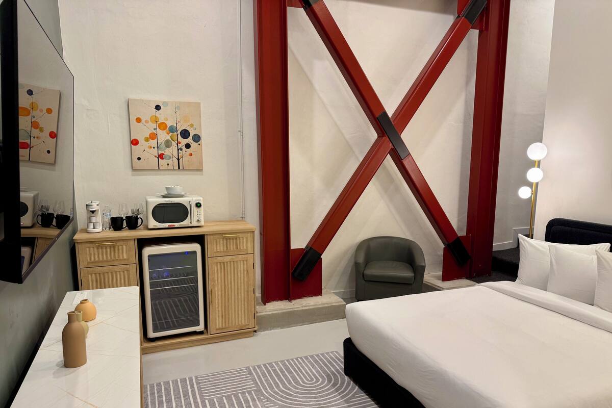 Habitación de hotel con cama, escritorio con microondas, refrigerador, silla y tocador con espejos.