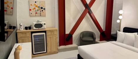 Habitación de hotel con cama, escritorio con microondas, refrigerador, silla y tocador con espejos.