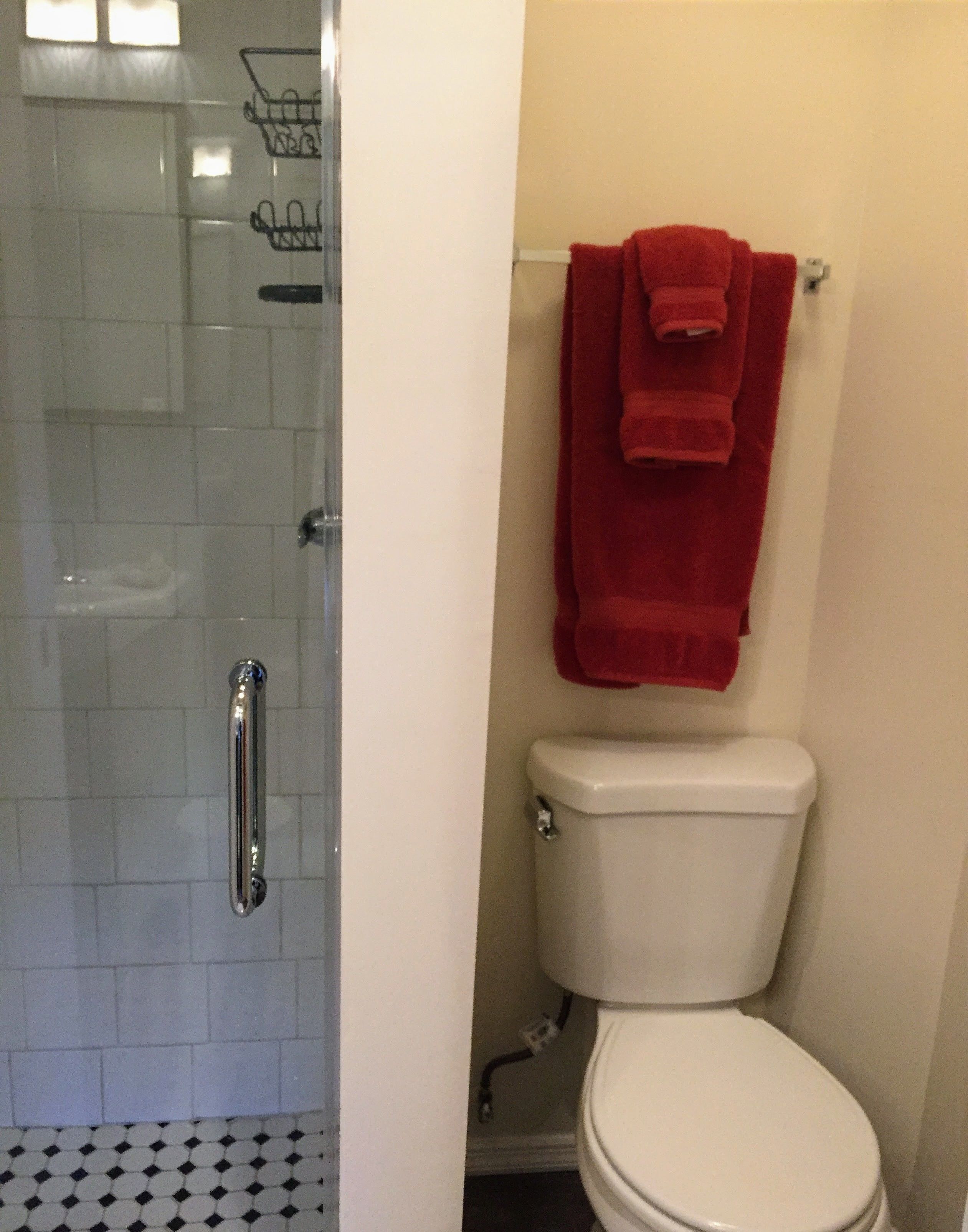 A bathroom with a white toilet, a red towel hanging on the wall, and a shower area with a glass door.