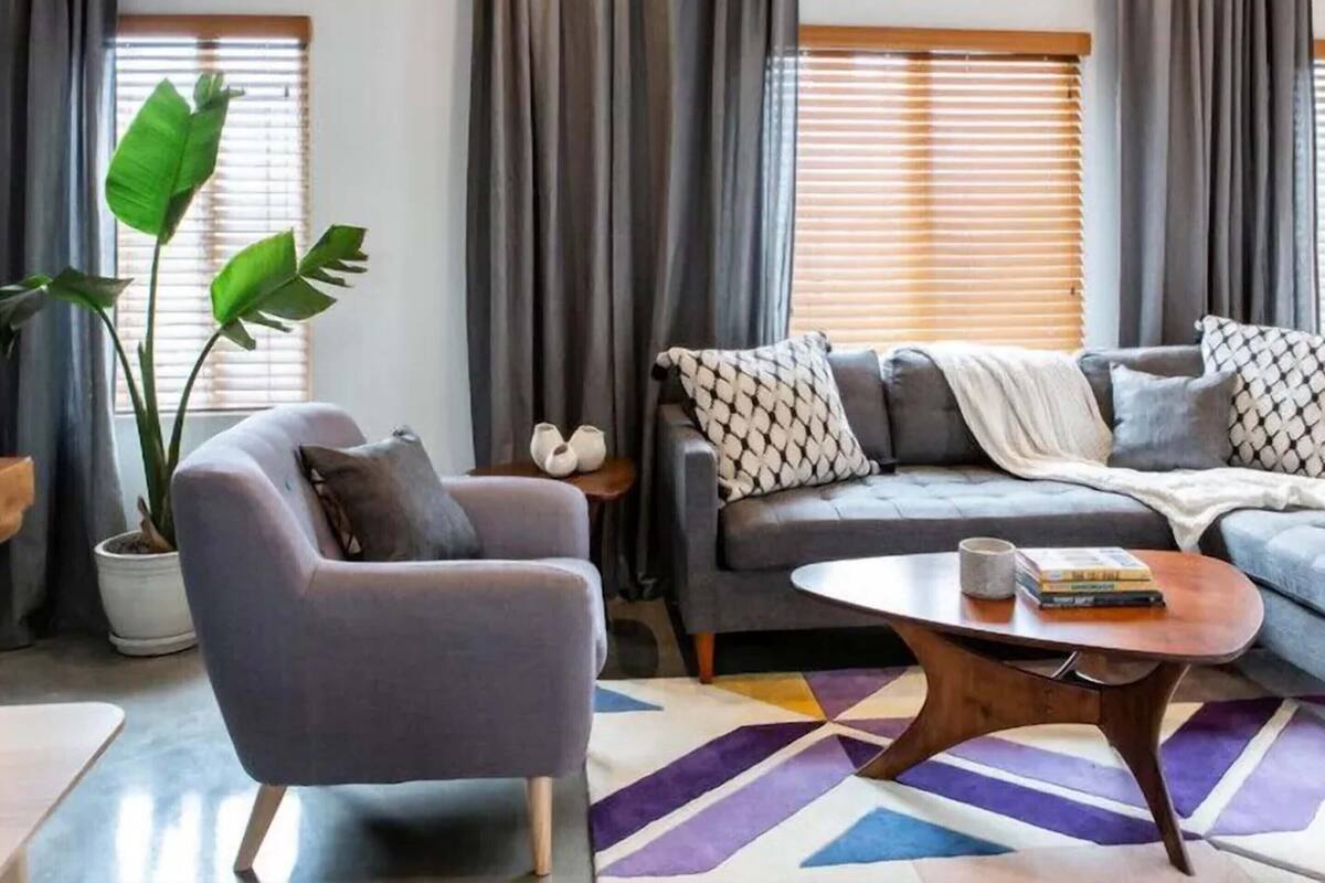 Una sala de estar con un sofá gris, un sillón gris, una mesa de centro y una planta grande.