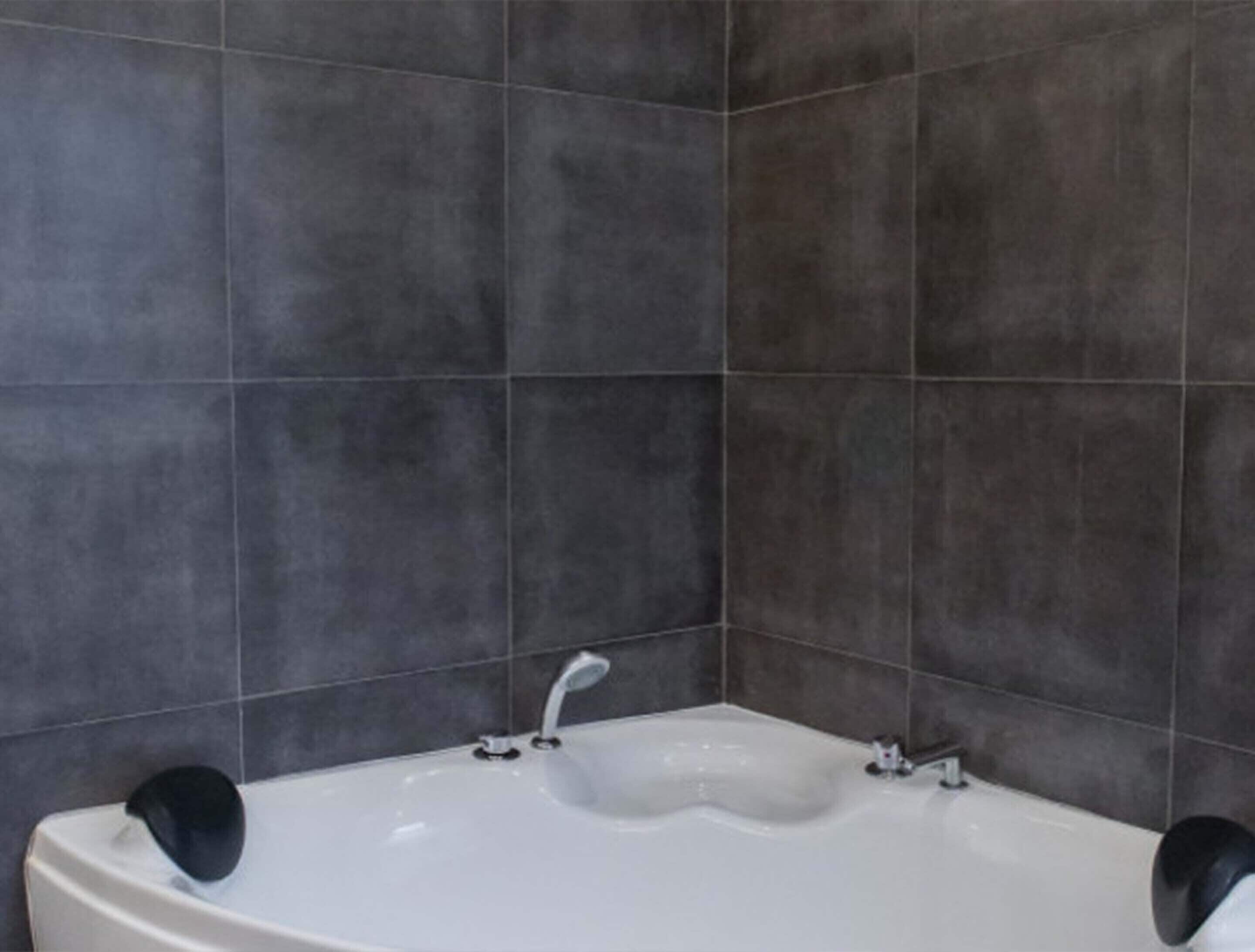 A bathroom with a white bathtub, dark grey tiles, and two black towel holders.