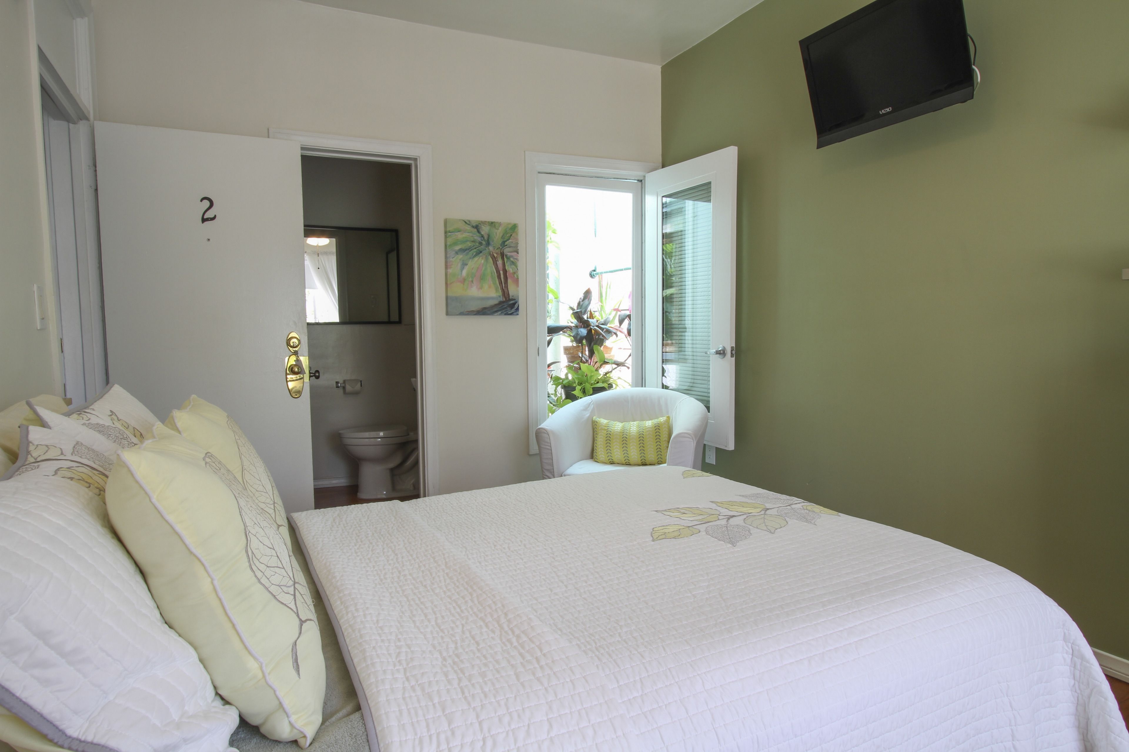 A bedroom with a bed, a door labeled '2', a toilet, a chair, and a TV mounted on the wall.