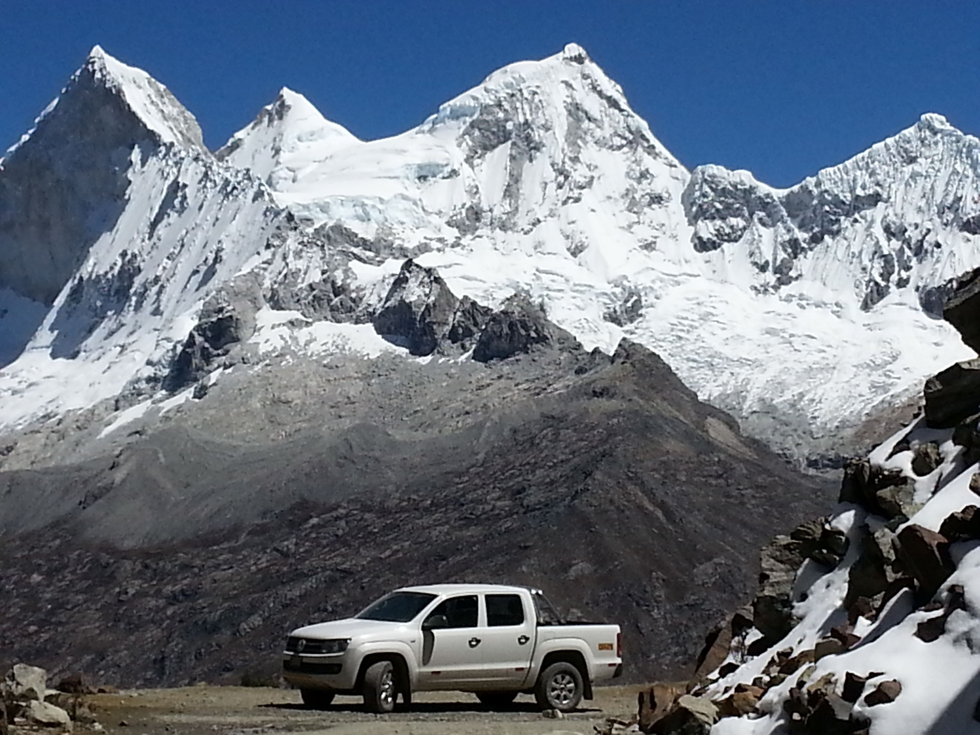 A white pickup truck parked in front of a snow-covered mountain range.