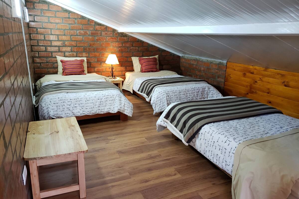 Um quarto de sótão acolhedor com três camas, um banco de madeira e uma parede de tijolos.