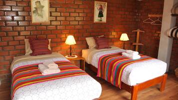 Una habitación con dos camas, cada una con un colorido edredón y almohadas a rayas, una pared de ladrillo y un piso de madera.