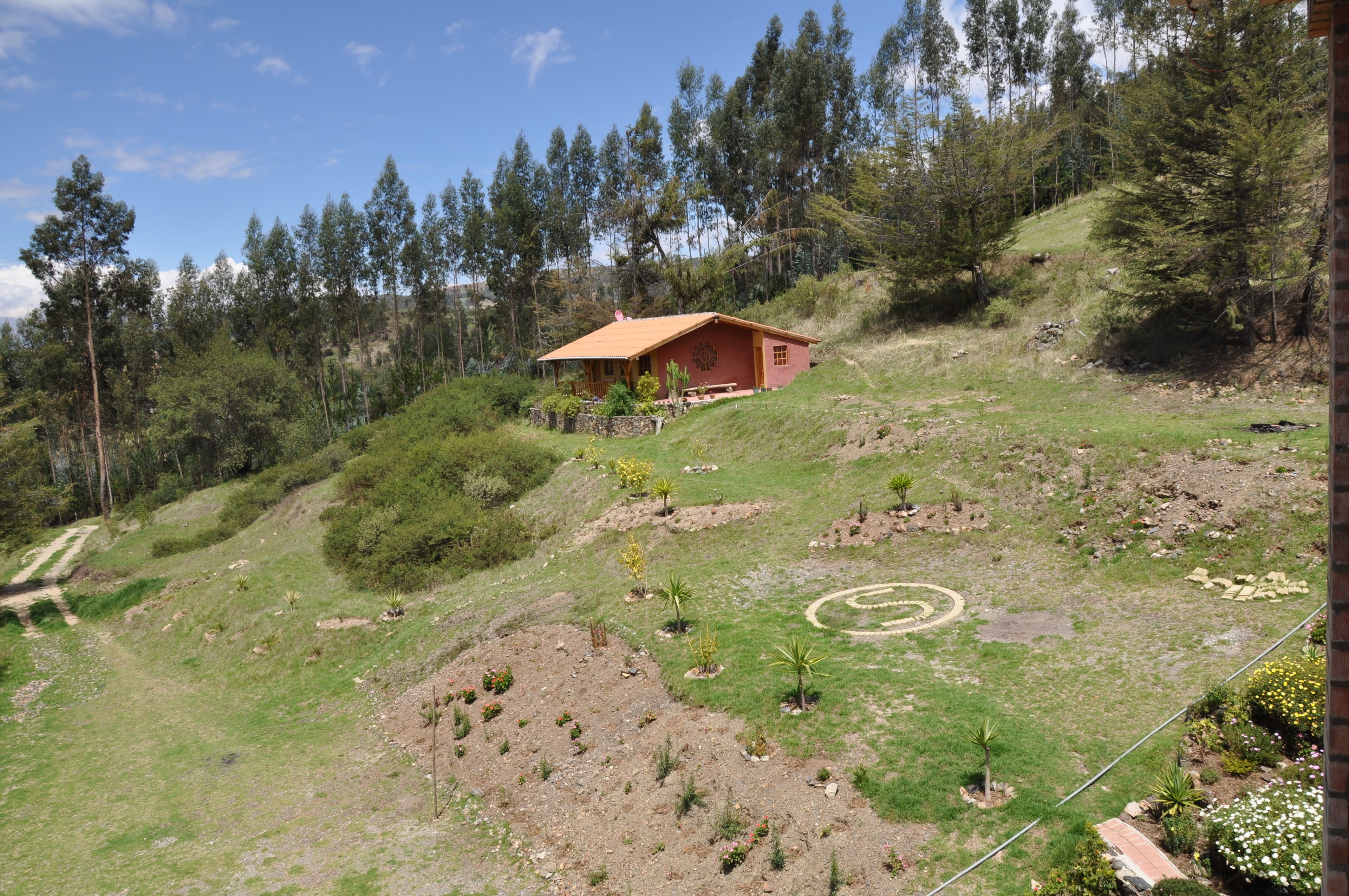 A hillside house with a red roof, surrounded by trees and a grassy landscape.