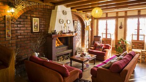 A cozy living room with a brick fireplace, wooden furniture, and a large window. - Copacabaña Lodge (Carhuaz)
