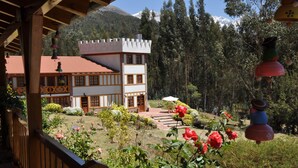 A traditional chalet with a red roof, surrounded by a well-maintained garden with red flowers and a view of a forested mountain range. - Copacabaña Lodge (Carhuaz)
