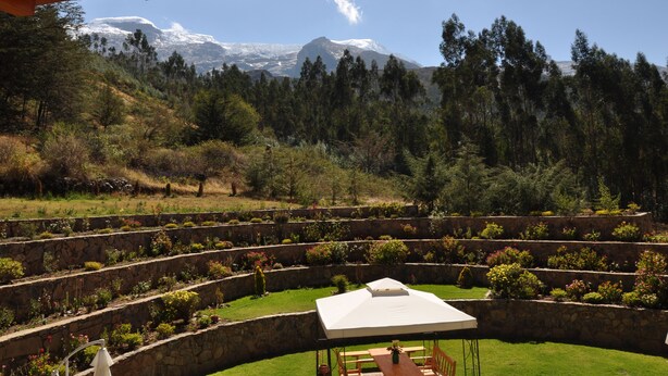 A landscaped garden with tiered flower beds and a table with chairs under a canopy, overlooking a mountainous landscape. - Copacabaña Lodge (Carhuaz)