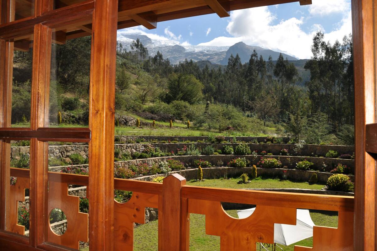Uma pérgula de madeira com vista para um jardim paisagístico e montanhas ao fundo.