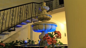Een meerlaags stenen fontein met een zwart ijzeren hekwerk en blauwe verlichting, omringd door potplanten en bloemen.