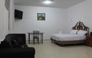 A bedroom with a bed, a chair, a table, and a painting on the wall.