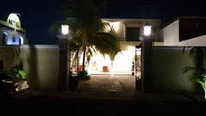 Een hotelingang 's nachts, met een palmboom voorop en een verlicht bord boven de ingang.