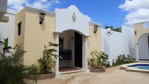 A building with a white facade, a central arched entrance, and a pool area with potted plants.