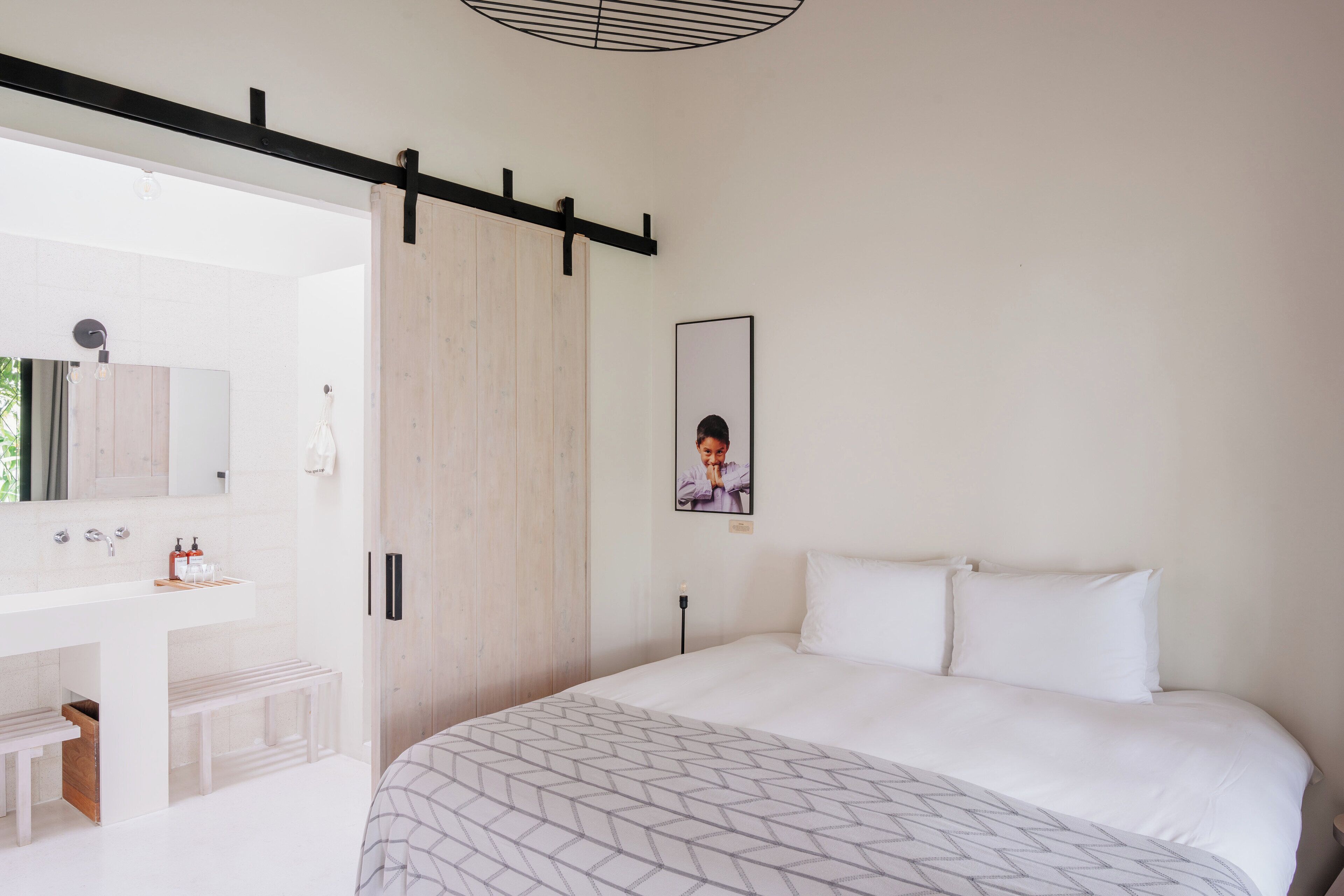 Un dormitorio moderno con una cama grande, un armario de madera, un baño blanco con lavabo y espejo, y un cuadro enmarcado en la pared.
