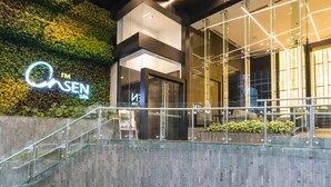 A modern building with a glass facade, a visible entrance, and a staircase leading to an upper level. - I’M Hotel (Makati)
