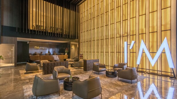 A modern hotel lobby with leather sofas, a reception desk, and a large illuminated 'I'M' sign. - I’M Hotel (Makati)