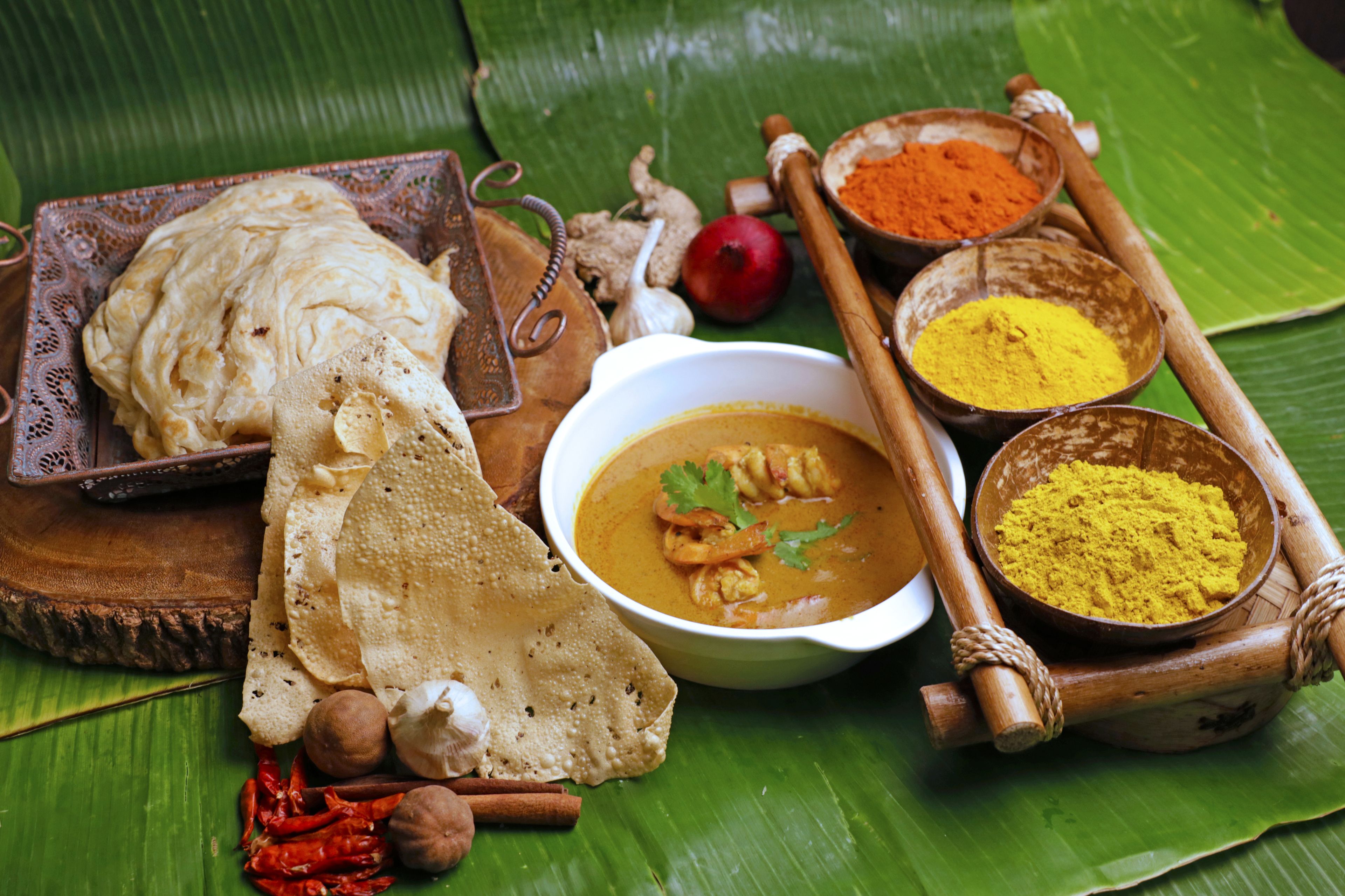 Presentación tradicional de comida con panes planos, un cuenco de curry y diversas especias sobre una hoja de plátano.