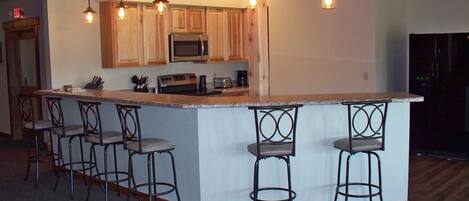 A kitchen with wooden cabinets, a stainless steel microwave, a stove, and a bar area with stools.