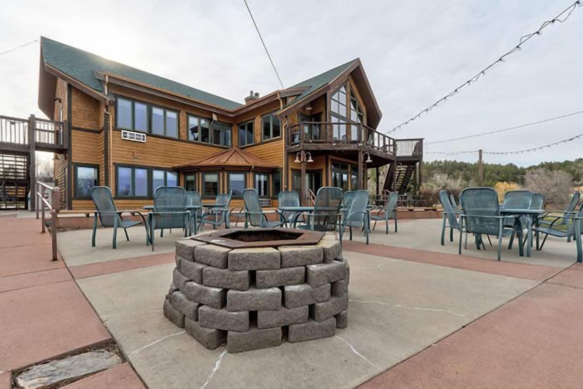 Un chalet doté d’un foyer en pierre, d’un espace salon extérieur et d’un grand bâtiment en bois avec de nombreuses fenêtres et un balcon.