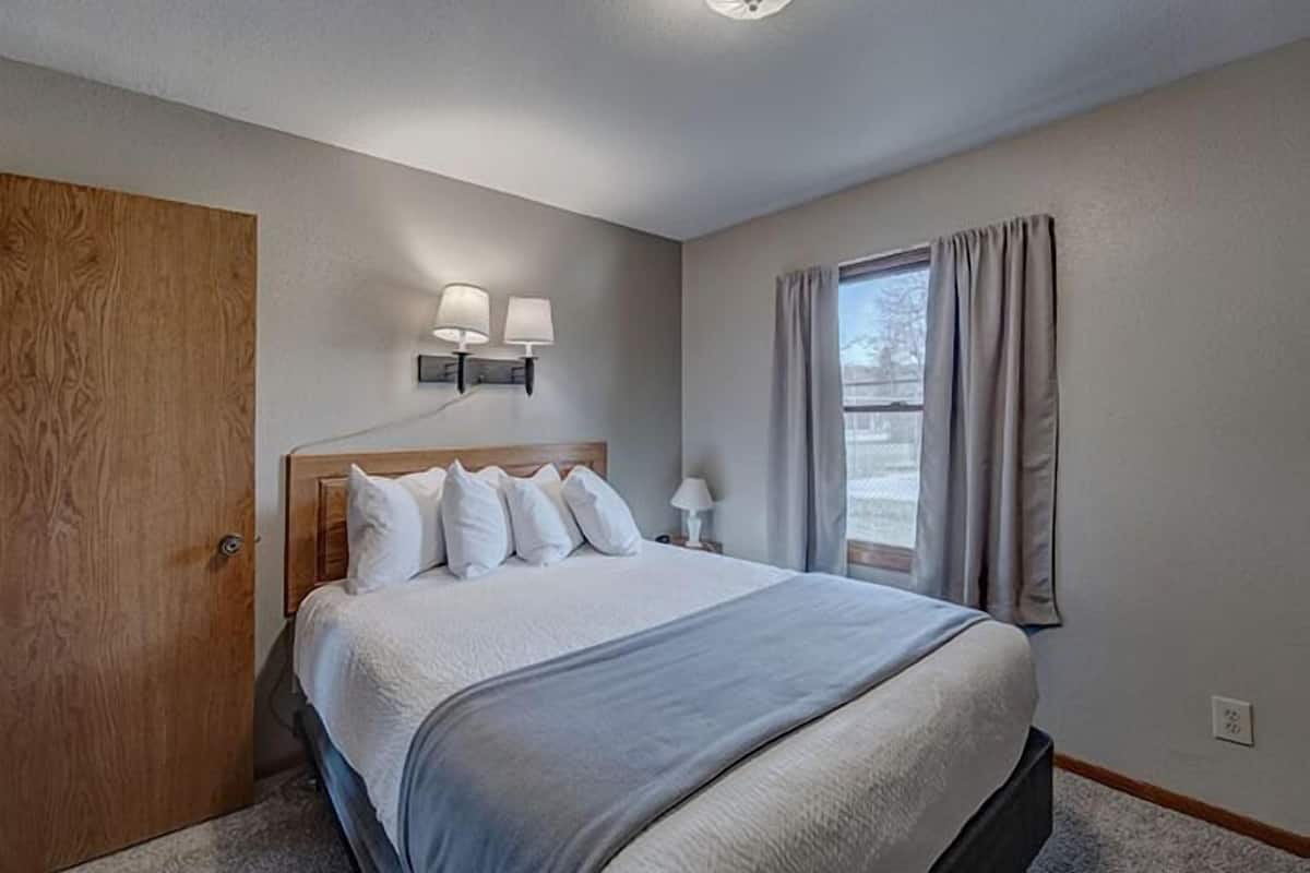 Une chambre à coucher avec un grand lit, une porte en bois, une table de chevet avec des lampes et une fenêtre avec des rideaux.
