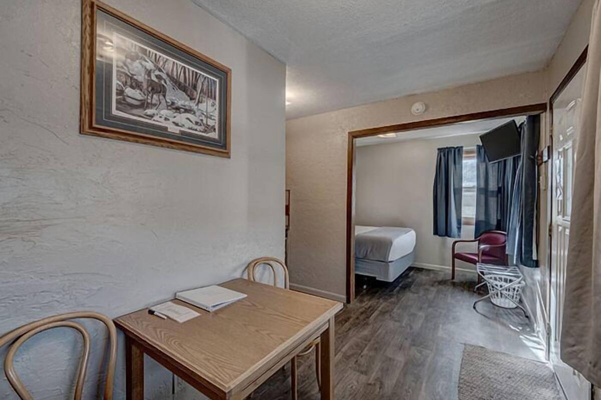 Une pièce avec une table en bois, un tableau encadré au mur, un lit recouvert d’une couverture bleue et une chaise.
