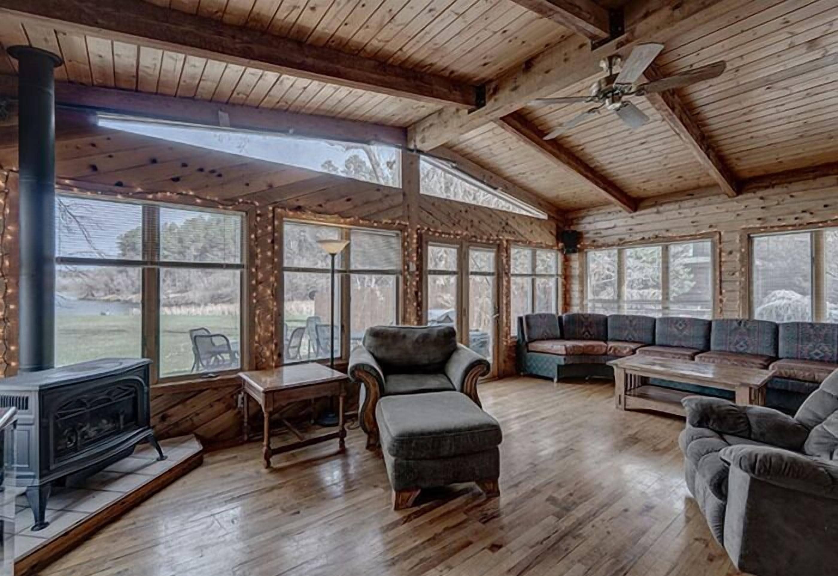 A cozy cabin interior with a fireplace, wooden furniture, and large windows offering views of the outdoors.
