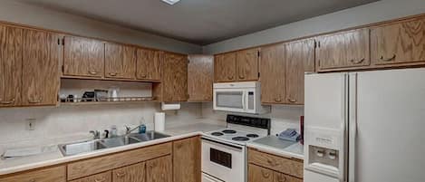 A kitchen with wooden cabinets, a microwave, a stove, and a refrigerator.