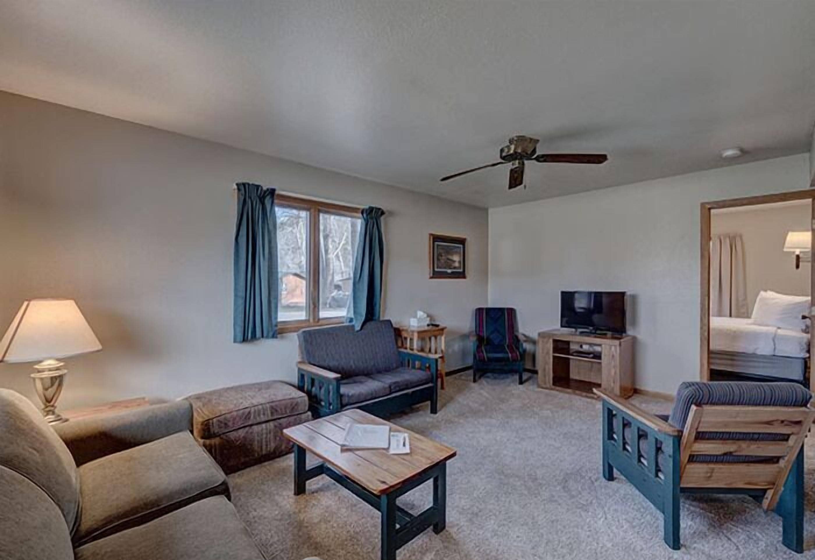 A hotel room with a sofa, armchair, wooden coffee table, TV stand, and a bed.
