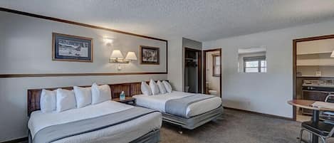 Habitación de hotel con dos camas, un escritorio, una silla, perchero y kitchenette.