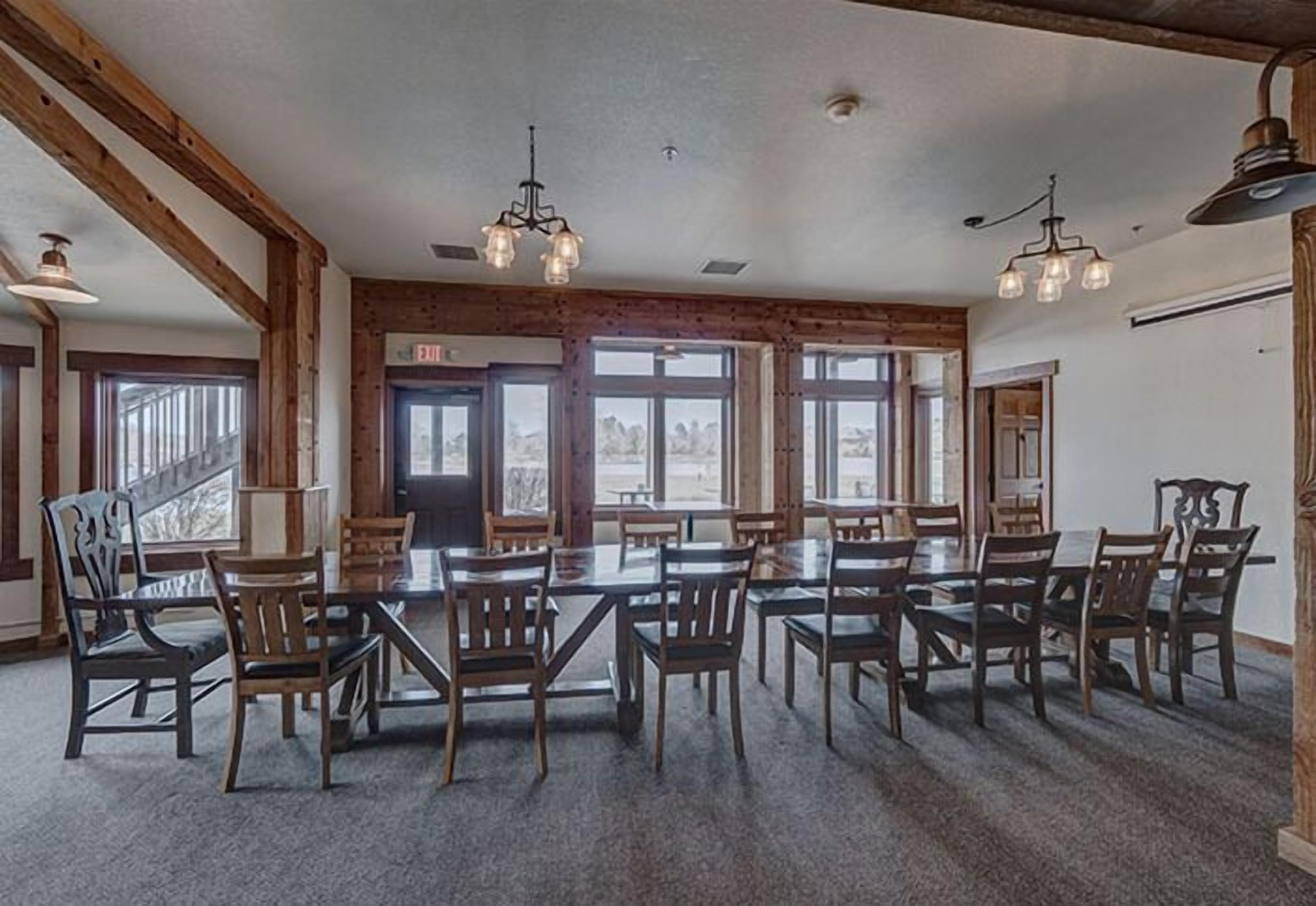 A spacious dining area with multiple tables and chairs, wooden beams on the ceiling, and large windows providing natural light.