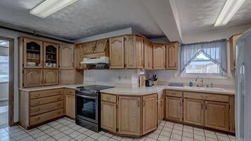 A kitchen with wooden cabinets, a stove, and a window with curtains.