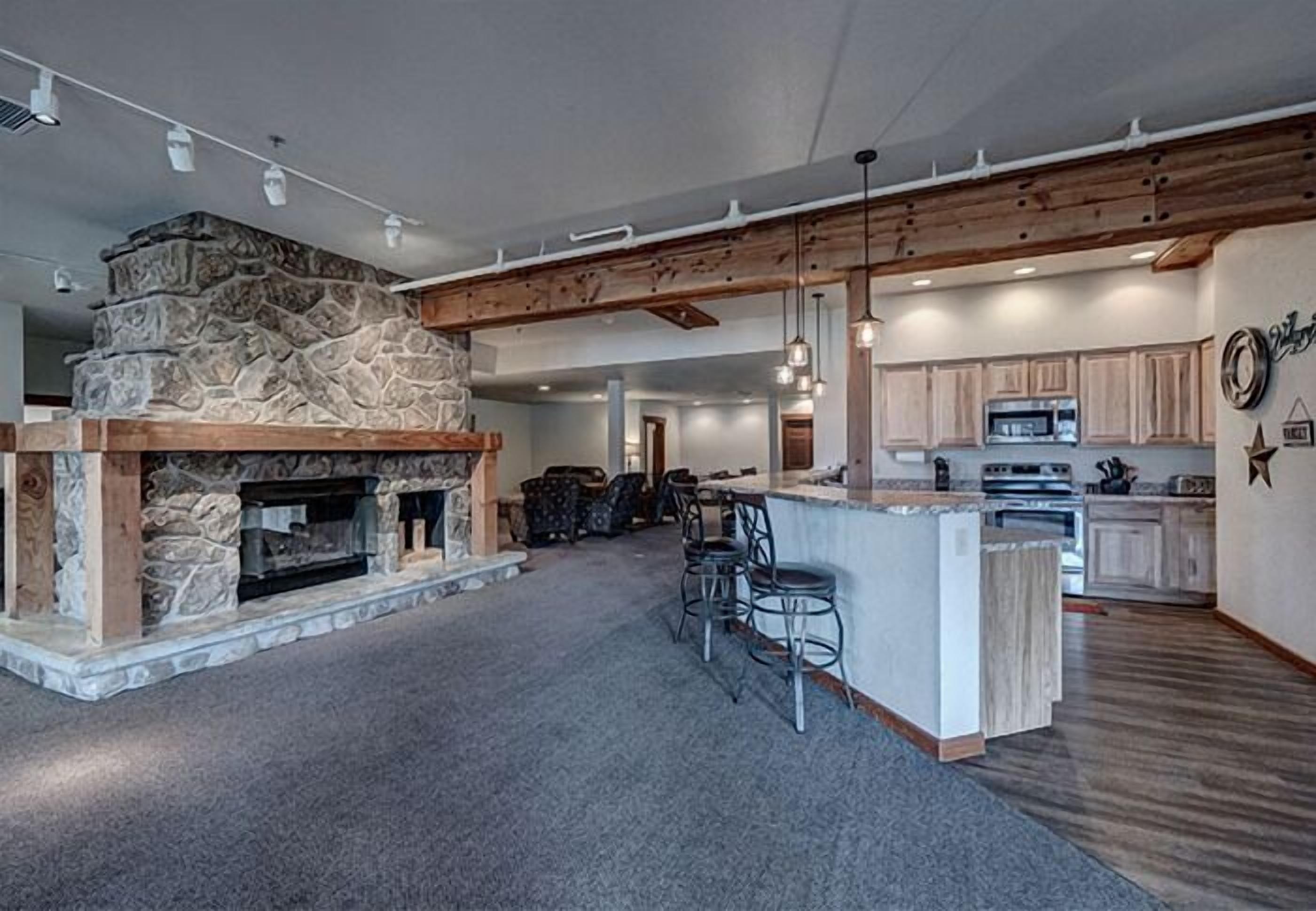 A spacious kitchen with a stone fireplace, wooden beams, and a bar area.