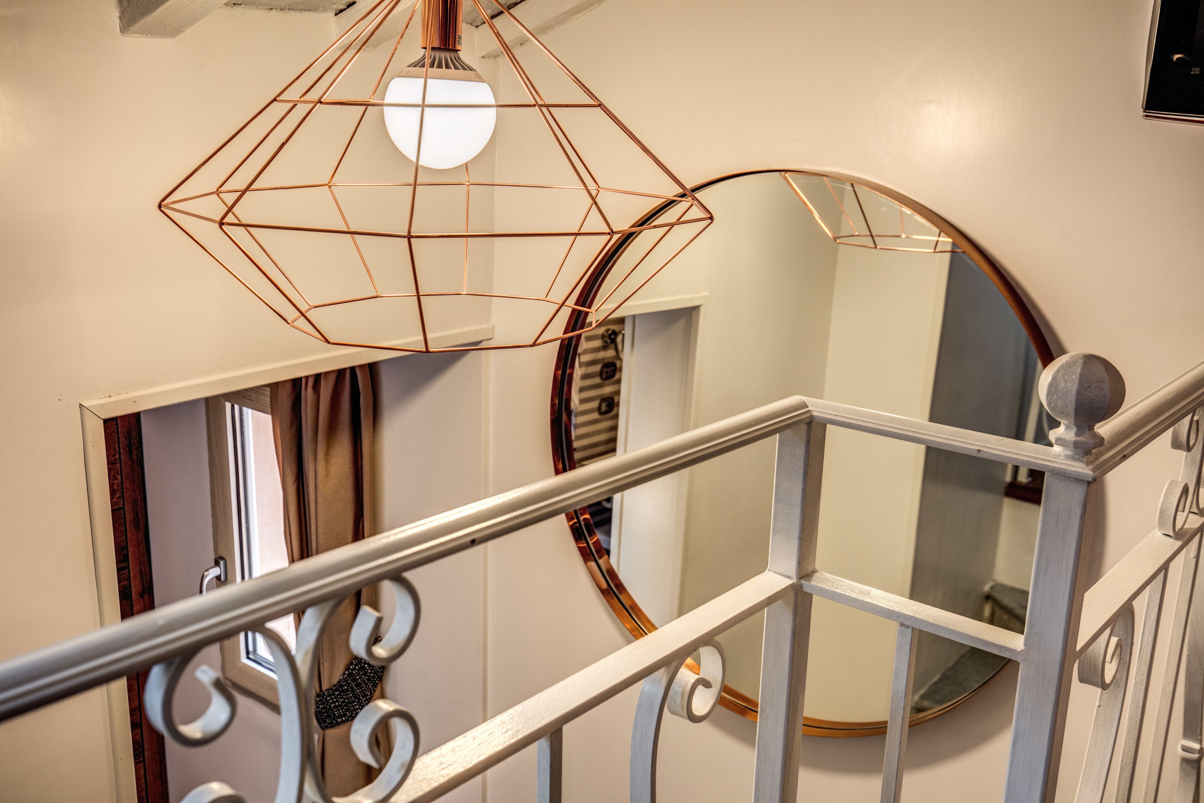 Een trap met een witte leuning en een geometrische hanglamp.