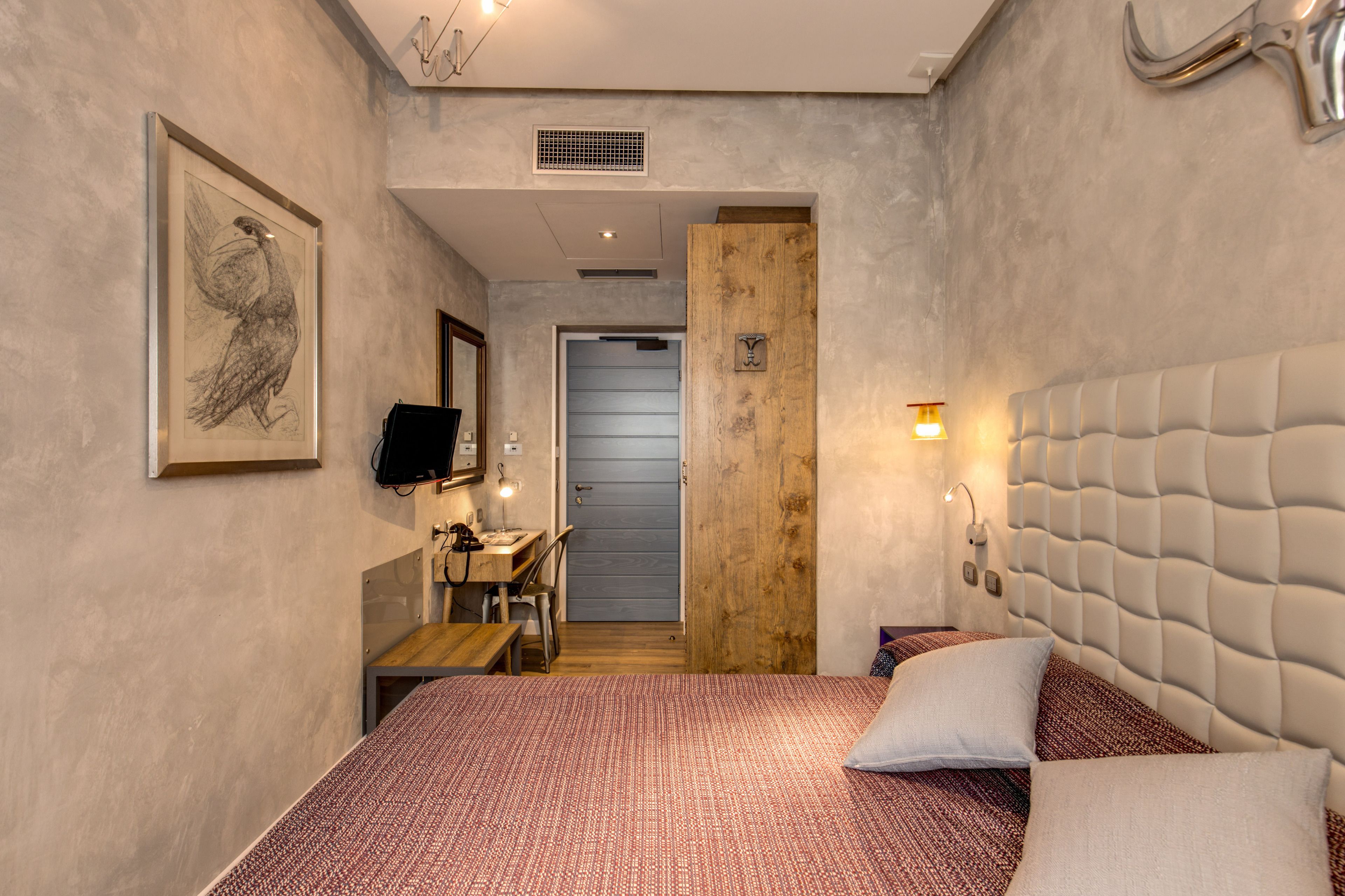 A bedroom with a bed, a desk, a chair, a television, and a door leading to another room.