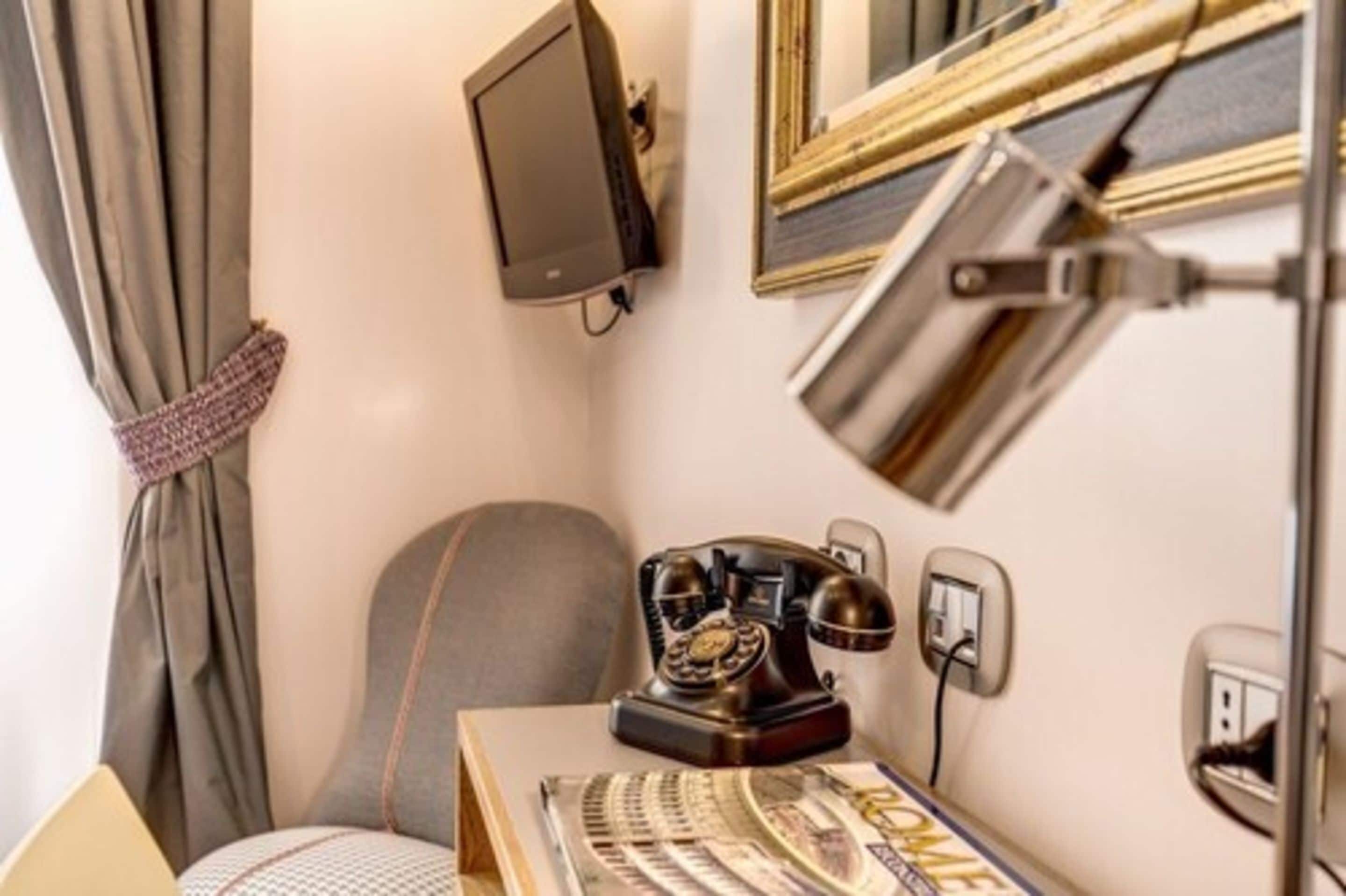 A room with a desk, a telephone, a television mounted on the wall, and a mirror.