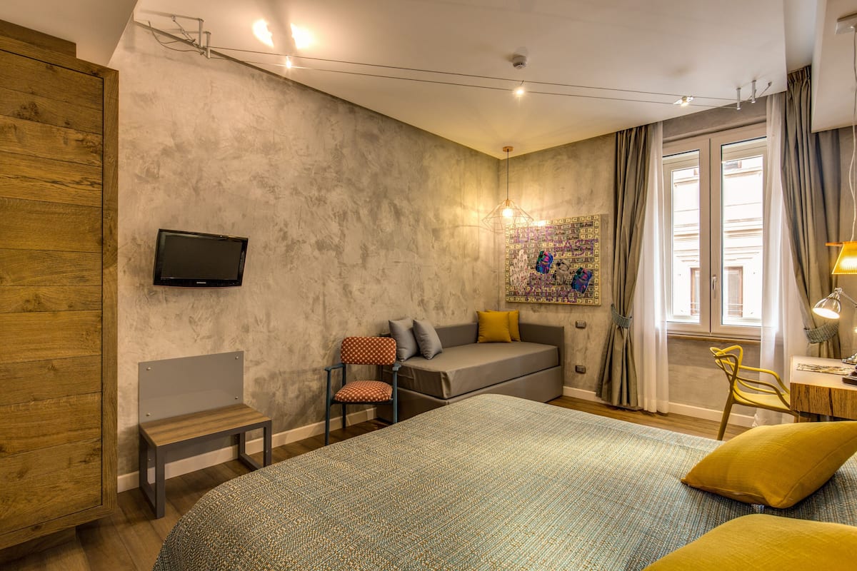 A bedroom with a bed, a desk, a chair, a television, and a window with curtains.