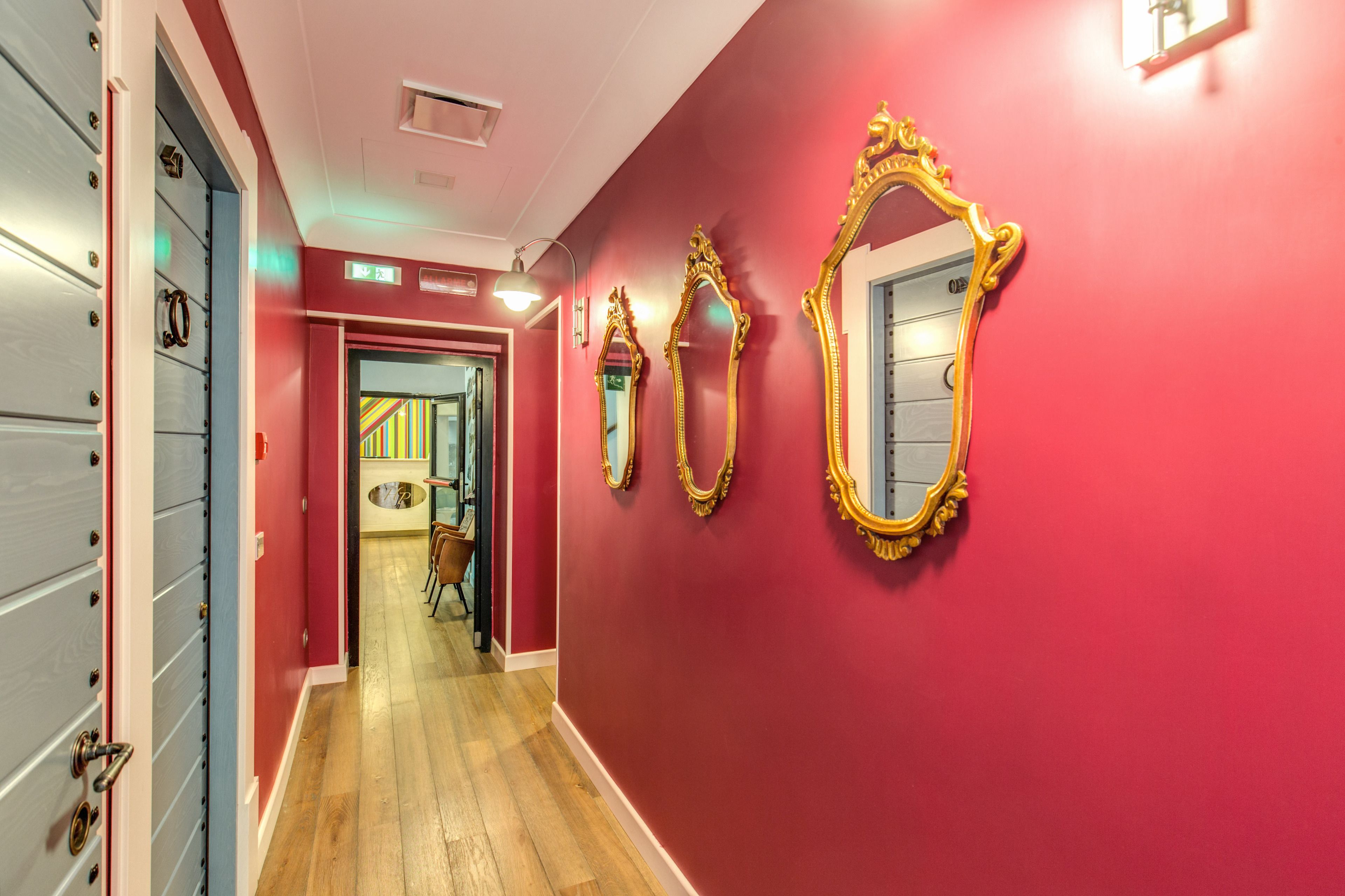 A hallway with red walls, wooden floors, and three ornate mirrors.