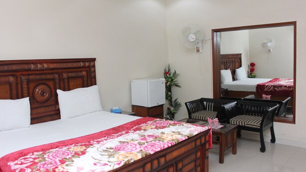 A hotel room with a wooden bed, a desk with a chair, a mirror, and a wall-mounted fan. - Hotel Royal Palace (Karachi)