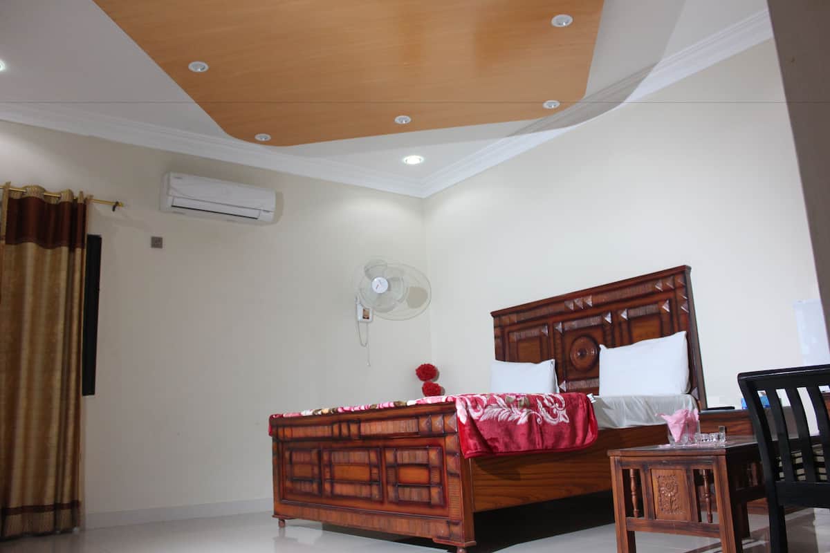 Un dormitorio con una cama de madera, una mesita de noche, una silla, un ventilador y un equipo de aire acondicionado.