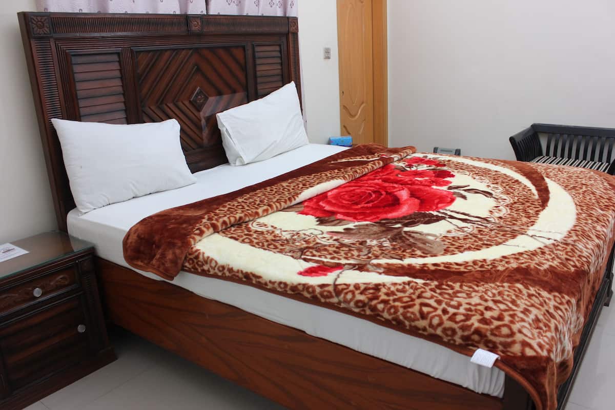 Una cama con un edredón estampado, un cabecero de madera y dos almohadas blancas.