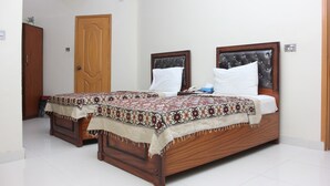A double bed with a patterned bedspread, a wooden headboard, and a bedside table with a lamp. - Hotel Royal Palace (Karachi)
