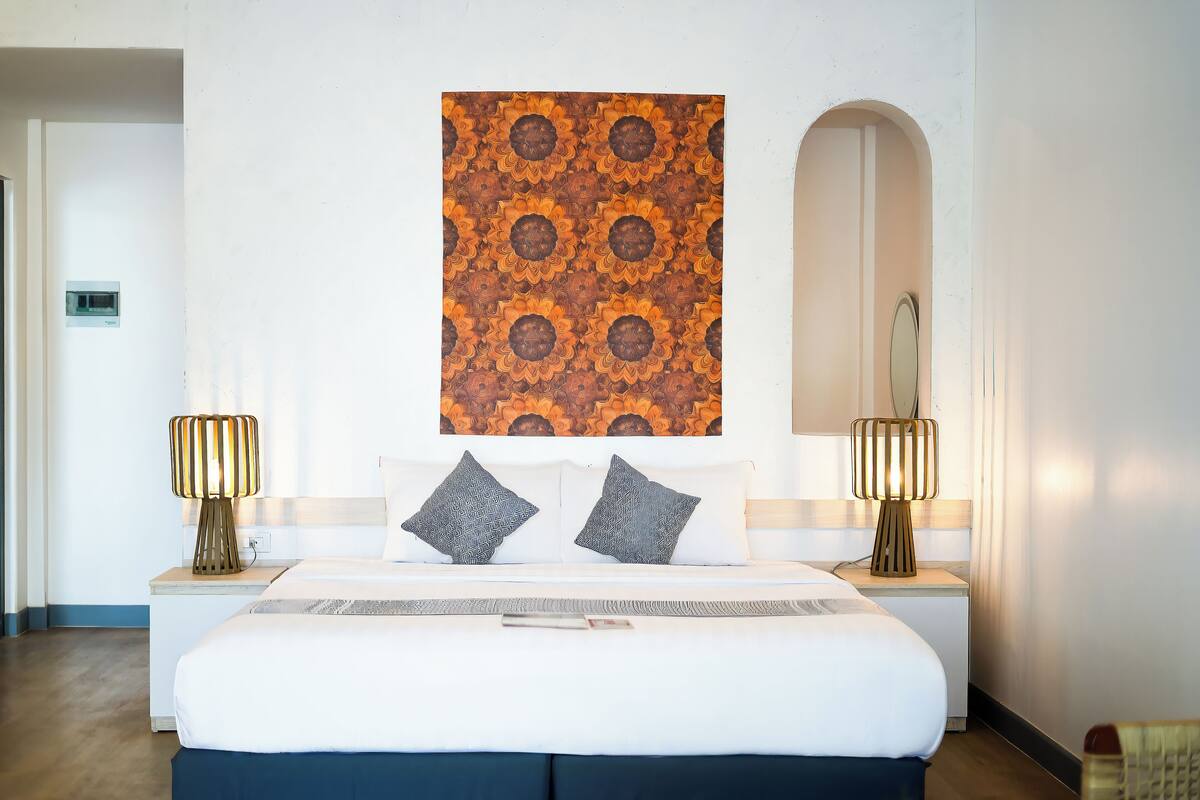 Habitación de hotel con una cama grande, dos lámparas de noche, una obra de arte en la pared y un espejo.