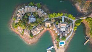 Eine Luftaufnahme eines Resorts mit einer kreisförmigen Anordnung von Villen, einem zentralen Pool und einem Steg.