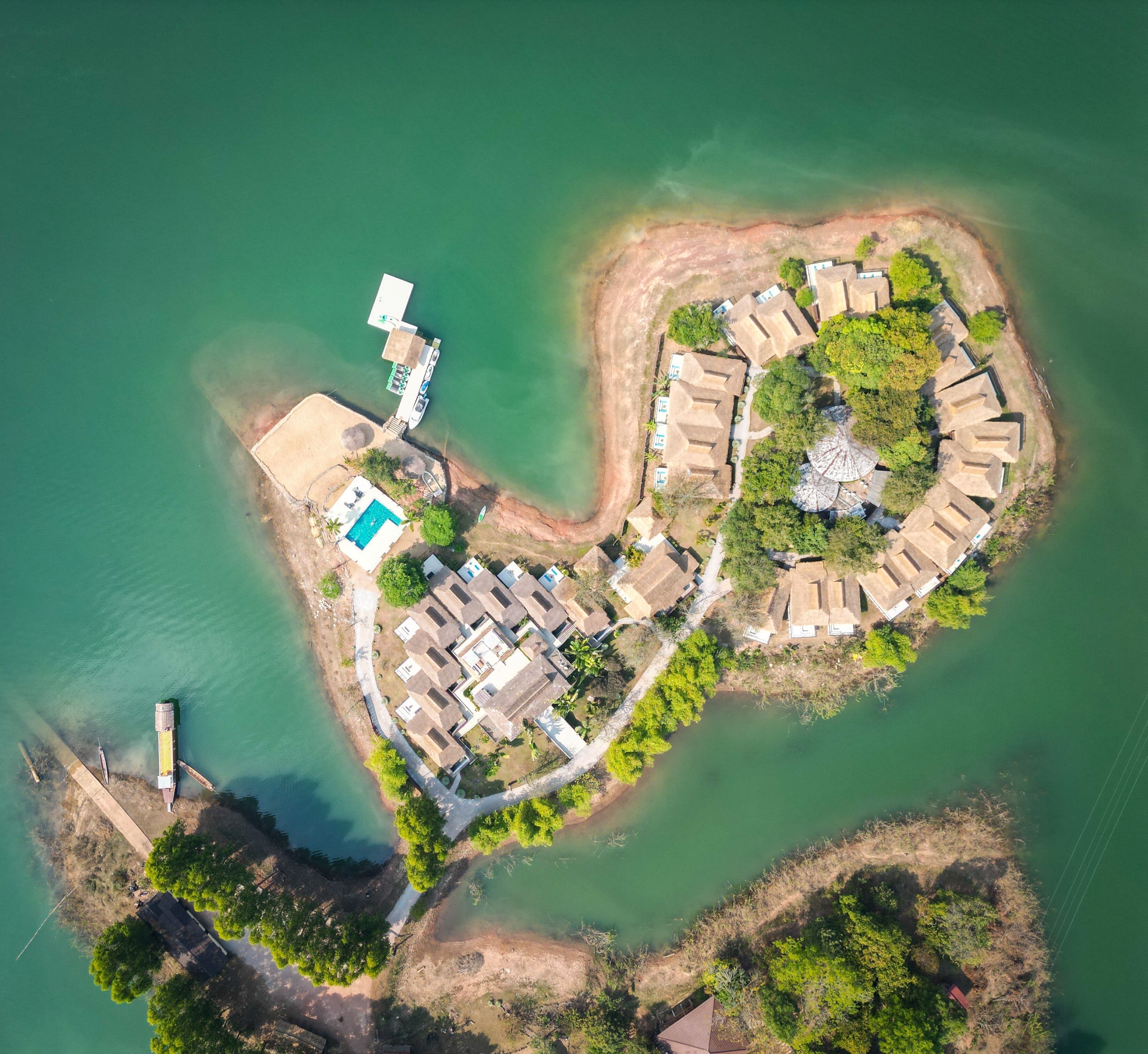 Vista aerea di un'isola resort con piscina, diverse sistemazioni in stile bungalow e un molo.
