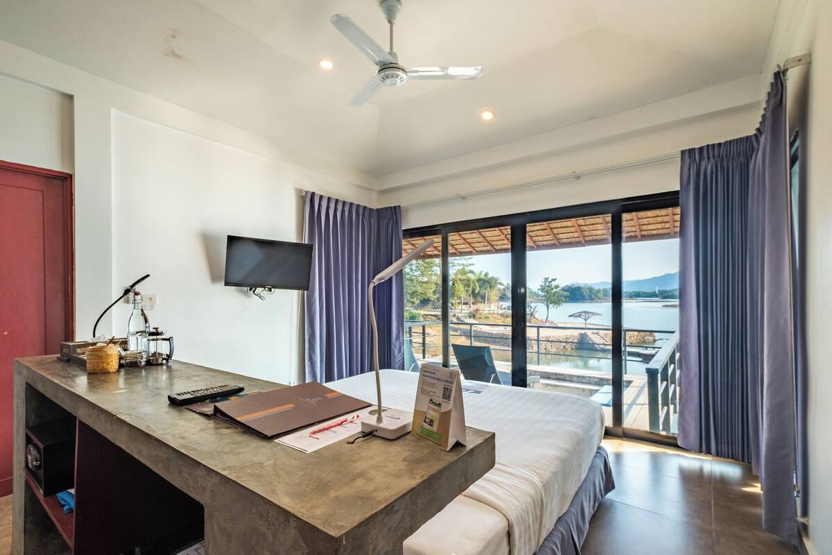 Habitación de hotel con una cama grande, un escritorio con ordenador, televisor y vista a un cuerpo de agua.