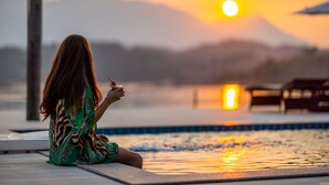 Eine Person sitzt am Pool während des Sonnenuntergangs, im Hintergrund Berge.