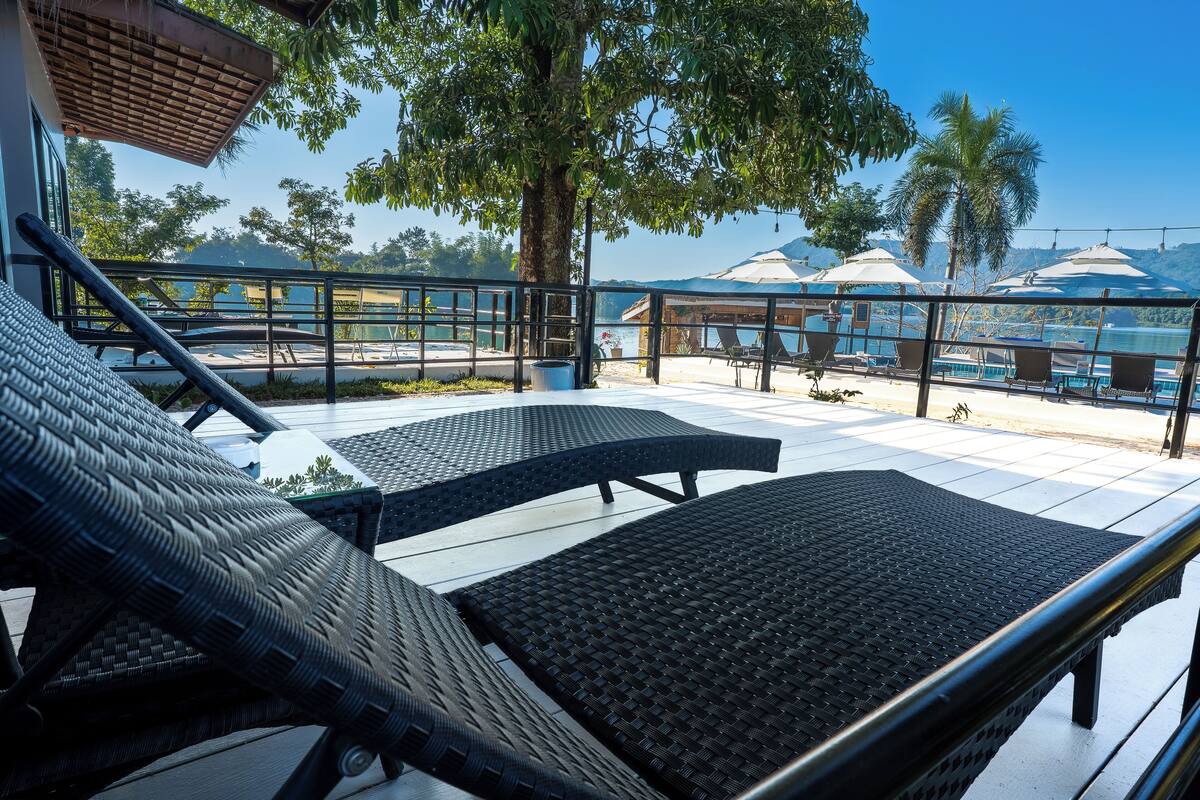 Una terraza con sillones de mimbre, vistas al agua y sombrillas.