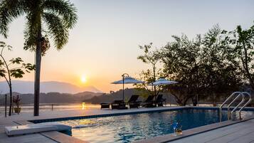 Relax by the serene pool surrounded by lush greenery and distant mountains.