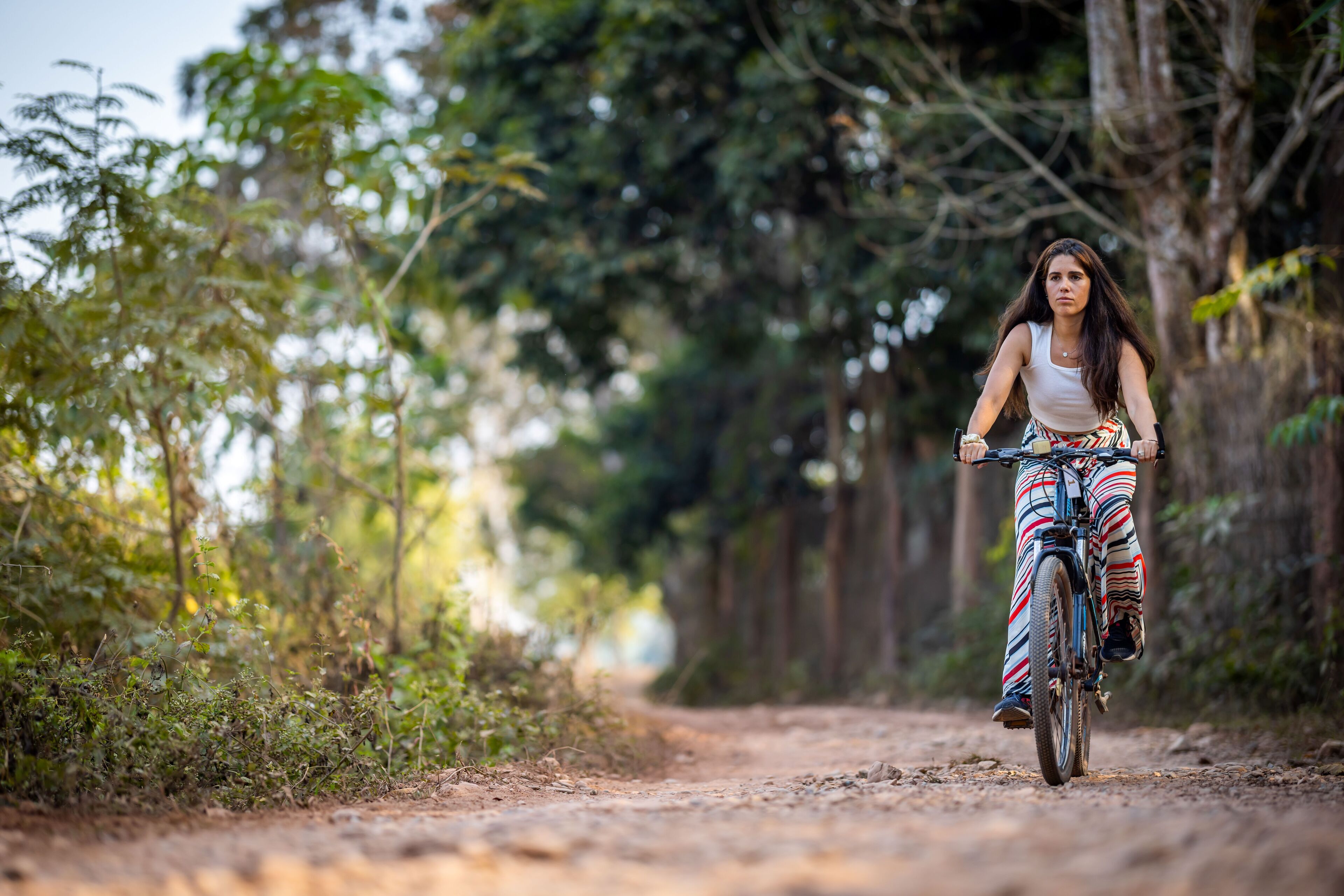 A person riding a bicycle on a dirt path surrounded by greenery.